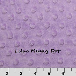 May include: A lilac minky fabric featuring a raised dot texture across the surface. The text "Lilac Minky Dot" is printed in the center. A white ruler with black markings is visible at the bottom, measuring up to 8 inches.