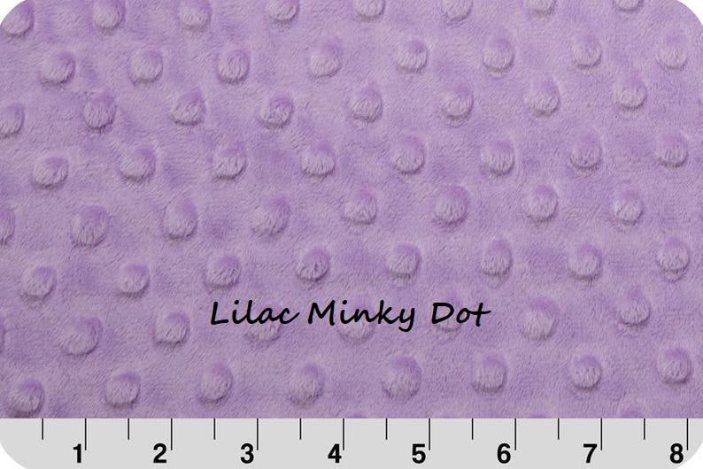 May include: A lilac minky fabric featuring a raised dot texture across the surface. The text "Lilac Minky Dot" is printed in the center. A white ruler with black markings is visible at the bottom, measuring up to 8 inches.