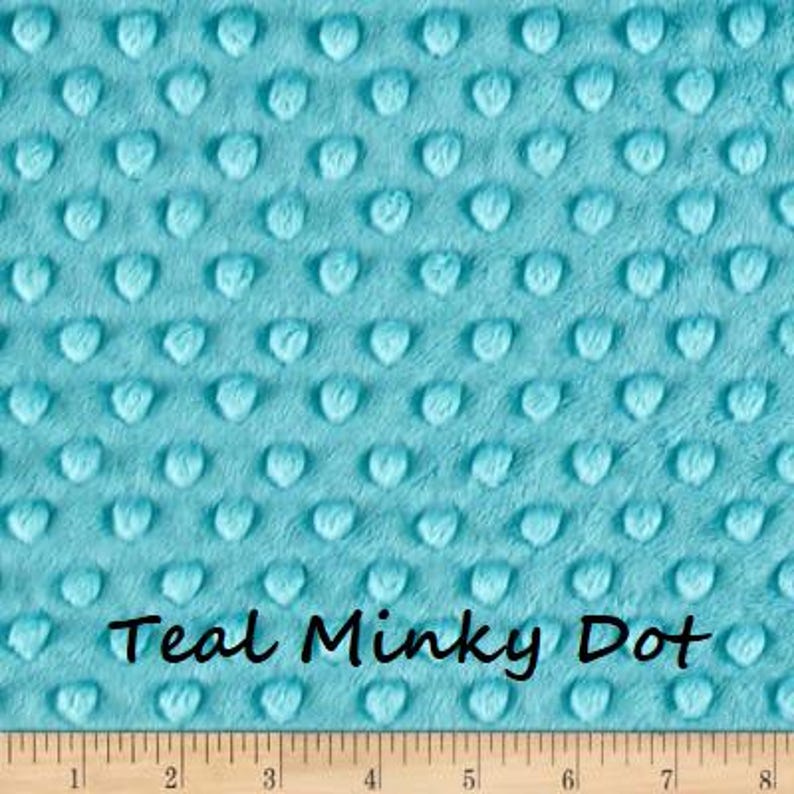 Pu&ograve; includere: Tessuto Teal Minky Dot con superficie strutturata. Il tessuto presenta un motivo di punti a forma di cuore in rilievo. Il testo "Teal Minky Dot" &egrave; scritto in corsivo nero nella parte inferiore del tessuto. Un righello di legno &egrave; in basso.