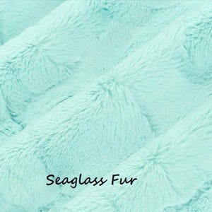 May include: A soft, plush fabric with a dense, long-pile texture in a light mint green color. The material features a wavy, rippled surface pattern throughout. The text "Seaglass Fur" is printed in a simple black font in the lower center area.