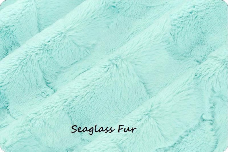 May include: A soft, plush fabric with a dense, long-pile texture in a light mint green color. The material features a wavy, rippled surface pattern throughout. The text "Seaglass Fur" is printed in a simple black font in the lower center area.