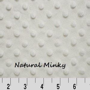 May include: Cream-colored minky fabric with a textured, dotted pattern. The fabric has a soft, plush appearance. The words "Natural Minky" are printed on the fabric. A ruler is at the bottom of the image.