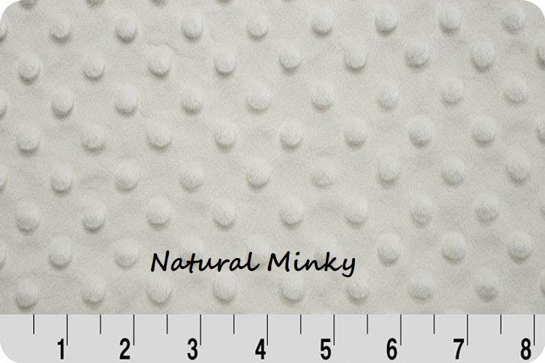 May include: Cream-colored minky fabric with a textured, dotted pattern. The fabric has a soft, plush appearance. The words "Natural Minky" are printed on the fabric. A ruler is at the bottom of the image.