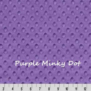 May include: A close-up of a purple minky dot fabric with a textured surface. The fabric has a repeating pattern of raised dots. The text "Purple Minky Dot" is written across the fabric. A ruler is at the bottom.