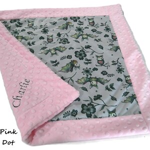 May include: A rectangular baby blanket featuring a light gray center panel with a repeating pattern of owls, bats, and dark flowers. The blanket has a textured blush pink minky dot border, with the name Charlie embroidered in black script.