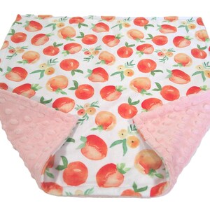 May include: A baby blanket with a white background featuring a pattern of watercolor peaches in shades of orange and red, with green leaves and yellow flowers. The blanket has a soft, pink, textured border.