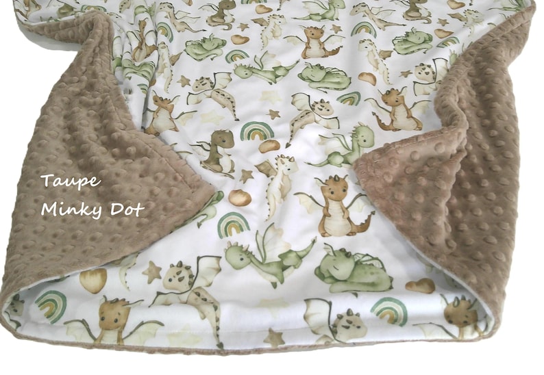 May include: A baby blanket with a white background featuring a pattern of cartoon dragons in shades of green, brown, and tan. The blanket has a taupe minky dot border. The text "Taupe Minky Dot" is visible.