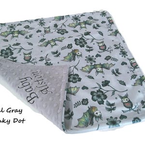 May include: A light gray baby blanket featuring a repeating pattern of bats, owls, and dark flowers. The underside is a textured steel gray minky dot fabric with the embroidered text Baby Alston. The blanket is folded to show both sides.