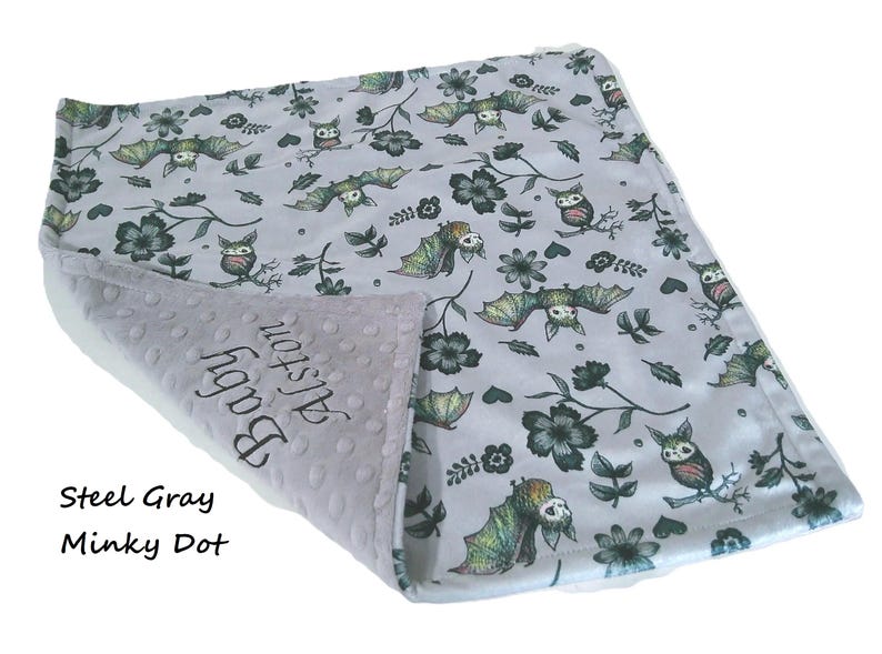 May include: A light gray baby blanket featuring a repeating pattern of bats, owls, and dark flowers. The underside is a textured steel gray minky dot fabric with the embroidered text Baby Alston. The blanket is folded to show both sides.