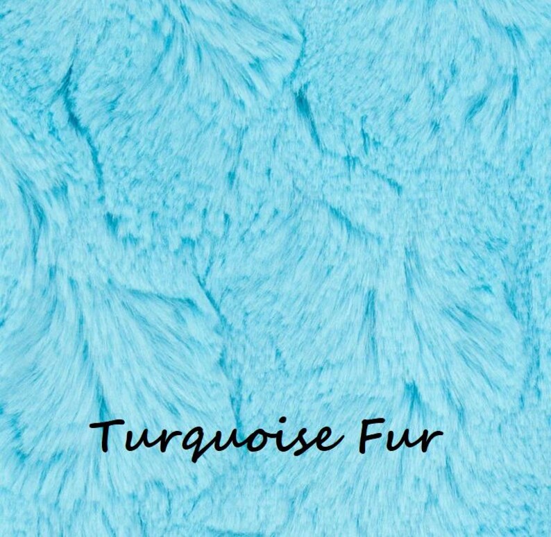 May include: A vibrant turquoise faux fur fabric with a dense, soft, and shaggy texture. The surface features long, flowing synthetic fibers in varying shades of bright blue and cyan. The text "Turquoise Fur" is printed in black in the center.