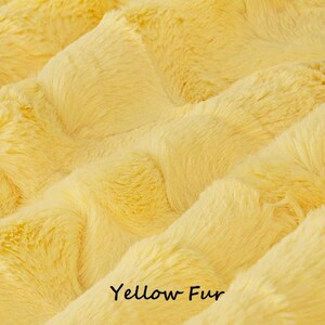May include: Close-up of a soft, yellow faux fur fabric. The fur is fluffy and has a wavy texture. The text "Yellow Fur" is printed at the bottom of the image.