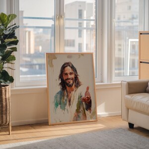 May include: A framed watercolor print of a man with long brown hair and a beard, wearing a white robe with blue and green accents. The man is smiling and extending his hand. The artwork is displayed in a well-lit room.