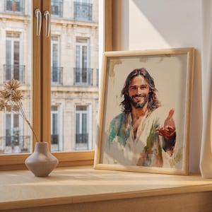May include: A framed watercolor print of a smiling man with long brown hair and a beard, wearing a white and blue robe. The artwork is in a light wooden frame and is displayed on a wooden surface.