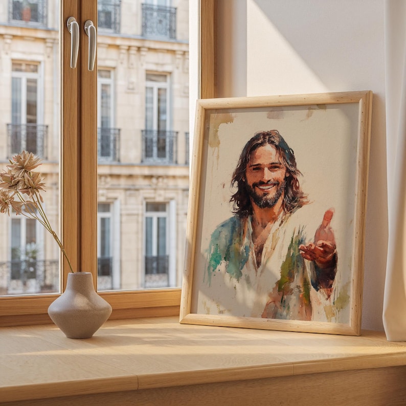 May include: A framed watercolor print of a smiling man with long brown hair and a beard, wearing a white and blue robe. The artwork is in a light wooden frame and is displayed on a wooden surface.