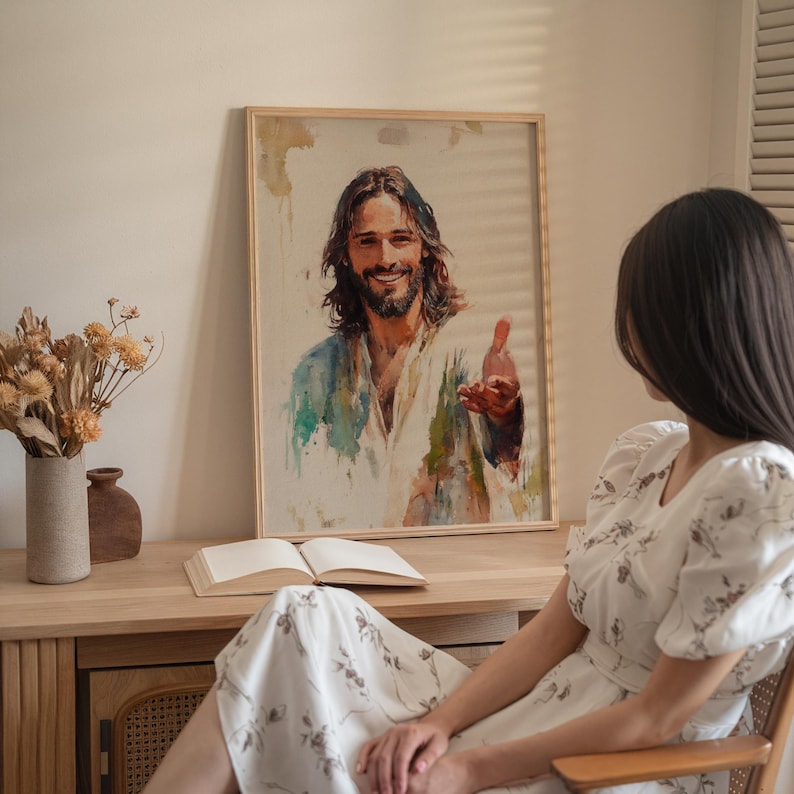 May include: A framed watercolor painting of a smiling man with long brown hair and a beard, wearing a white and blue robe. The painting is displayed on a wooden table with a book and vase.