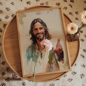 May include: A framed watercolor print of a smiling man with long hair and a beard, wearing a white and blue robe. A pink flower is in the foreground. The artwork is displayed on a wooden table with a vase of flowers.