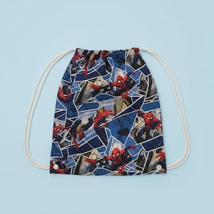 May include: A drawstring backpack featuring a repeating comic book style pattern of the character Spider-Man in red and blue suits. The bag has a dark blue background with geometric shapes and white cord straps attached at the bottom corners.