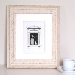 Może przedstawiać: Oprawiona czarno-biała ilustracja przedstawia postać w długim płaszczu i kapeluszu w oknie z kotem. Grafika znajduje się w białym passe-partout i białej drewnianej ramie. Po prawej stronie biała filiżanka i spodek.