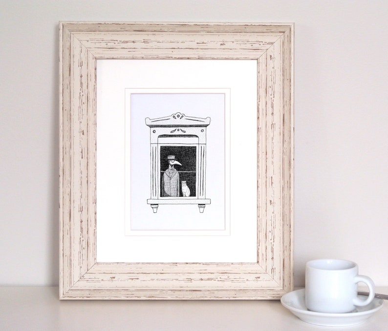 Może przedstawiać: Oprawiona czarno-biała ilustracja przedstawia postać w długim płaszczu i kapeluszu w oknie z kotem. Grafika znajduje się w białym passe-partout i białej drewnianej ramie. Po prawej stronie biała filiżanka i spodek.