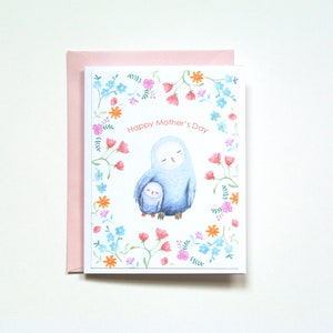 A baby owl is snuggling to it's mom, and mother is holding the baby under her wing.  They are surrounded by pretty small flowers.  The card says; Happy Mother's Day