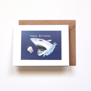 A scary looking big shark is sticking head out of sea and trying to eat a birthday cake.  The card says; Happy Birthday