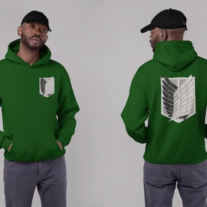 May include: Green hoodie with a front pocket and a black and white emblem on the chest and back. The hoodie has a hood and long sleeves. The person in the image is wearing a black baseball cap and gray pants.