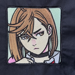 May include: Embroidered patch featuring an anime-style illustration of a woman with brown hair and a stern expression. The patch has a light green border and is set against a black background. The woman is wearing a black choker and hoop earrings.
