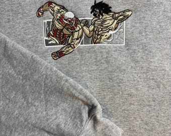 Könnte beinhalten: Grauer Kapuzenpullover mit einem gestickten Design von zwei muskulösen Figuren im Kampf. Die Figuren sind mit beigem, rotem und schwarzem Garn detailliert, das sich in einem weißen rechteckigen Rahmen befindet. Der Hoodie hat eine Kapuze mit Kordelzug und ein geripptes Bündchen.