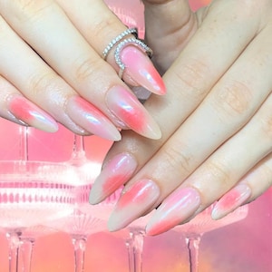 Peut inclure: Gros plan sur une main avec de longs ongles en ombré rose et blanc. Les ongles sont longs et pointus, et l'effet ombré est subtil. La main porte une bague en argent avec de petits diamants.