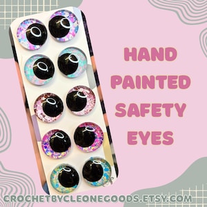 May include: Eight hand-painted safety eyes with black pupils and glitter in various colours. The eyes are displayed on a white card with the text "HAND PAINTED SAFETY EYES". The Etsy shop name is also visible.