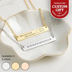 May include: Two personalised bar necklaces, one gold and one silver, on a white dish. The gold necklace reads "Miles apart but close at heart" with a state outline. The silver necklace displays coordinates. The image also shows "Available in 3 colours" and "CUSTOM GIFT".