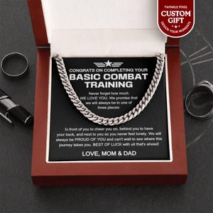 May include: A silver chain necklace displayed in a dark red gift box. The box contains a black card with the text "CONGRATS ON COMPLETING YOUR BASIC COMBAT TRAINING" and a message from "LOVE, MOM & DAD."