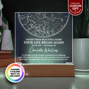 May include: A personalized LED night light with a wooden base. The acrylic panel displays a star map and text: "UNDER THESE BEAUTIFUL STARS YOUR LIFE BEGAN AGAIN" with a name and date. Features 3 modes and 7 colors.