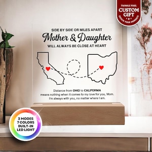 May include: A lighted acrylic sign with the text "Mother & Daughter" and the phrase "Will Always Be Close At Heart." The sign features outlines of California and Ohio, connected by a dotted line, with hearts. The base is wood, and the sign has a built-in LED light with 7 colors.