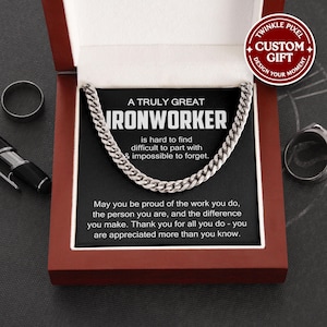 May include: A silver chain necklace presented in a red gift box. The box features a black card with the text "A TRULY GREAT IRONWORKER" and a message. A ring and pen are visible in the background. The gift box has a "Twinkle Pixel Custom Gift" logo.