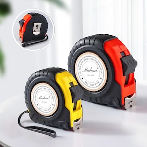 Puede incluir: Dos cintas métricas personalizadas, una roja y negra, la otra amarilla y negra. Cada una presenta una etiqueta circular con el nombre "Michael" y el texto "BEST DAD EVER". Las cintas métricas tienen una correa de muñeca negra y un clip de cinturón metálico.