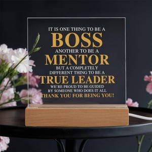 May include: A lighted acrylic plaque with a wooden base. The plaque has gold lettering on a black background that reads: "IT IS ONE THING TO BE A BOSS, ANOTHER TO BE A MENTOR, BUT A COMPLETELY DIFFERENT THING TO BE A TRUE LEADER."