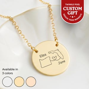 Op de afbeelding: Een goudkleurige ketting met een ronde hanger. De hanger heeft gegraveerde contouren van Oregon en Florida, met een hartsymbool en de namen "Eliza" en "Jane". De ketting is verkrijgbaar in drie kleuren. De tekst "AANGEPASTE CADEAU" is ook zichtbaar.