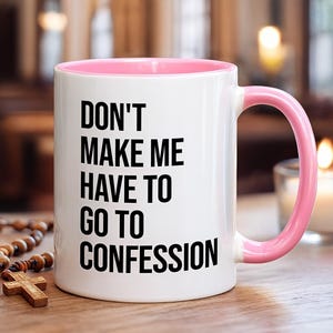 May include: White ceramic mug with a pink interior and handle. The mug features the black text: "DON'T MAKE ME HAVE TO GO TO CONFESSION". A wooden rosary and cross are visible in the background.