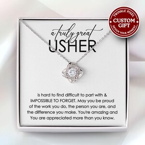Puede incluir: Un collar plateado con un colgante en forma de nudo, engastado con cristales transparentes, presentado en una caja de regalo blanca. La caja presenta el texto "a truly great USHER" y un mensaje. Una pegatina circular roja y blanca dice "CUSTOM GIFT".