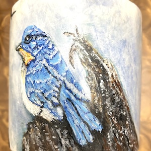 May include: A bluebird with white markings perched on a branch. The bird is painted on a white ceramic mug with a blue and white background.