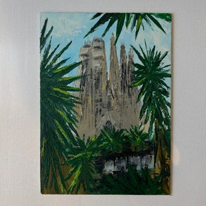 May include: An oil painting of the Sagrada Familia basilica in Barcelona, Spain. The artwork depicts the cathedral's intricate facade and spires, framed by lush green palm fronds against a light blue sky. The painting is on a white canvas.