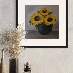 May include: A framed painting of sunflowers in a dark blue vase. The sunflowers have bright yellow petals and dark brown centers. The vase sits on a gray surface, and the background is a light blue and gray gradient.