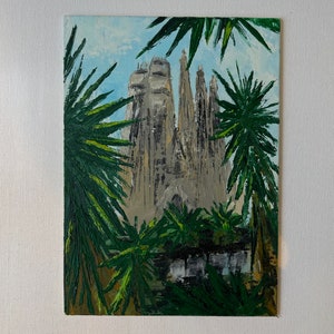 May include: An oil painting of the Sagrada Familia in Barcelona, Spain, framed by green palm fronds. The cathedral is depicted in shades of gray and beige against a light blue sky. The artwork is on a white canvas.