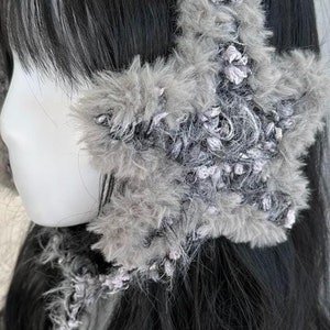 May include: Gray faux fur ear warmer with a star-shaped design. The ear warmer is made of soft, fluffy material and has a delicate, crocheted texture.