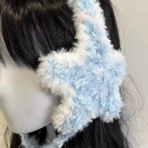 Può includere: Una fascia per paraorecchie soffice, azzurra, con copriorecchie a forma di stella. La fascia e i copriorecchie sono rifiniti con pelliccia bianca. Questo accessorio è progettato per tenere le orecchie al caldo e aggiungere un tocco di stile.