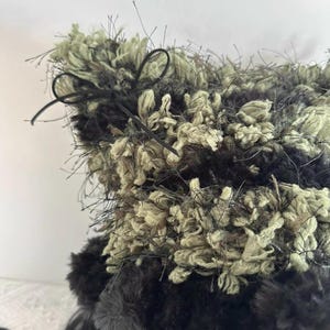 Puede incluir: Un sombrero texturizado hecho a mano con una mezcla de hilo negro, verde oliva y beige. El sombrero presenta un dise&ntilde;o esponjoso y peludo con un lazo de cinta negra. La textura y la paleta de colores &uacute;nicos del sombrero crean un accesorio elegante.