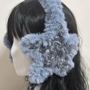 Könnte beinhalten: Ein Paar blaue Ohrenschützer aus Kunstfell mit einem sternförmigen Design. Die Ohrenschützer sind weich und warm, perfekt um die Ohren im Winter warm zu halten.