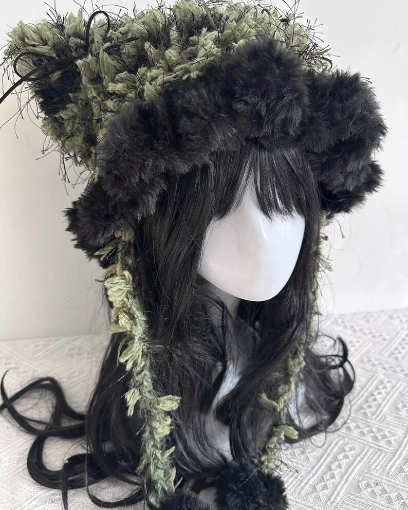 Puede incluir: Un tocado &uacute;nico con una combinaci&oacute;n de texturas y colores. El dise&ntilde;o incluye una banda esponjosa de color gris oscuro y una corona de material texturizado verde y negro. El pelo largo y oscuro enmarca la cara, con detalles verdes.