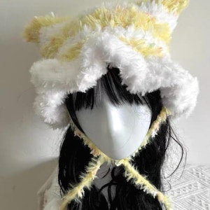 Puede incluir: Un sombrero hecho a mano con un diseño único. El sombrero presenta una combinación de piel sintética amarilla y blanca, con un borde con volantes y una parte superior puntiaguda. Una corbata a juego asegura el sombrero debajo de la barbilla. El sombrero está diseñado para ser usado.